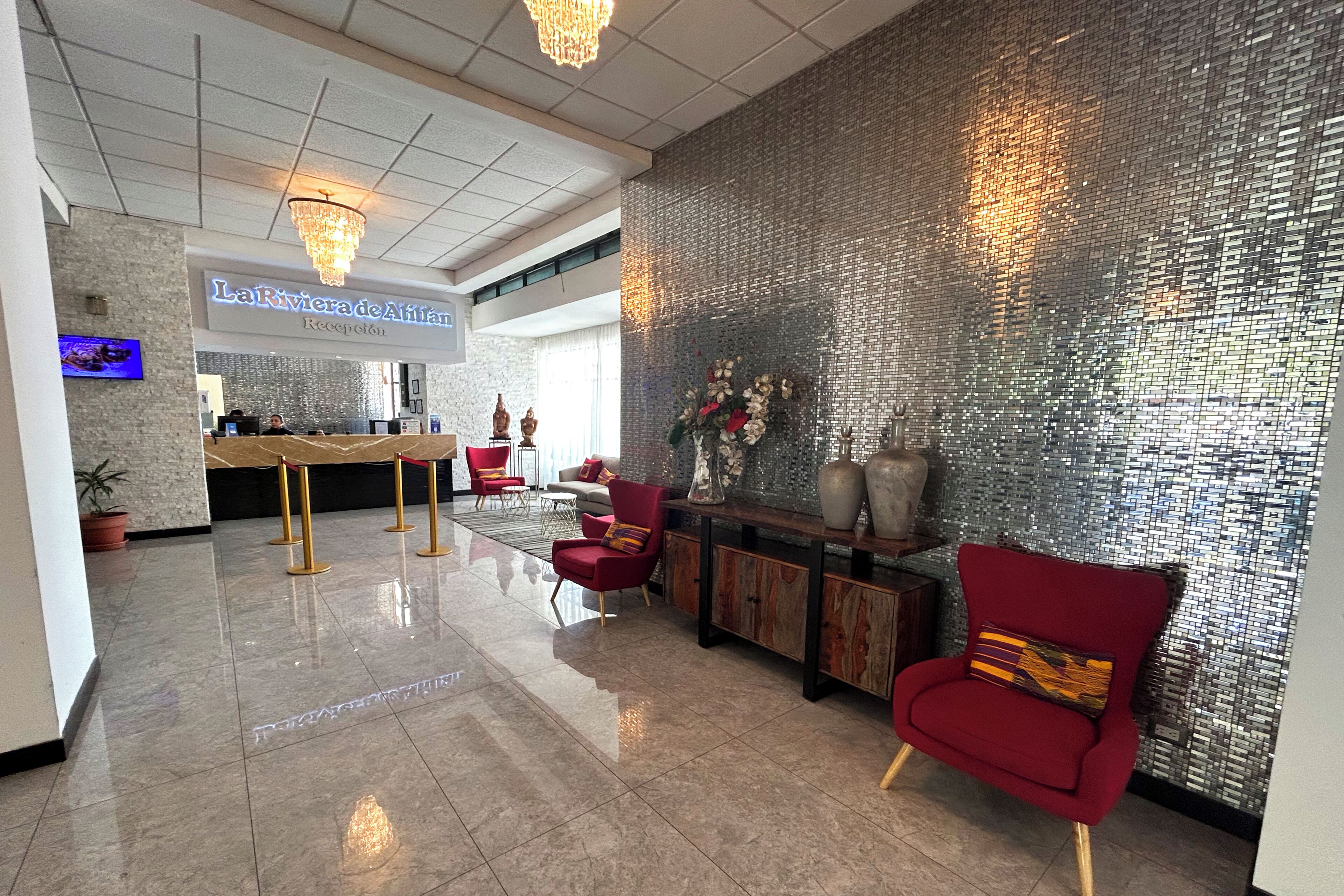 A reception area with a chandelier, a reception desk, red chairs, and a decorative wall.