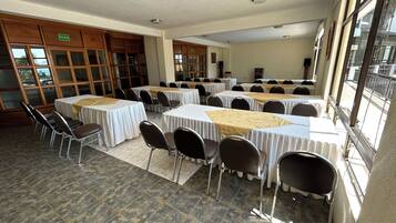 Una sala de conferencias con varias mesas y sillas, ventanas amplias y una puerta señalizada con 'SALIDA'.