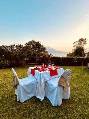 An outdoor dining setup with tables set for four, surrounded by greenery and a view of the sea. - Hotel La Riviera de Atitlan (Sololá)