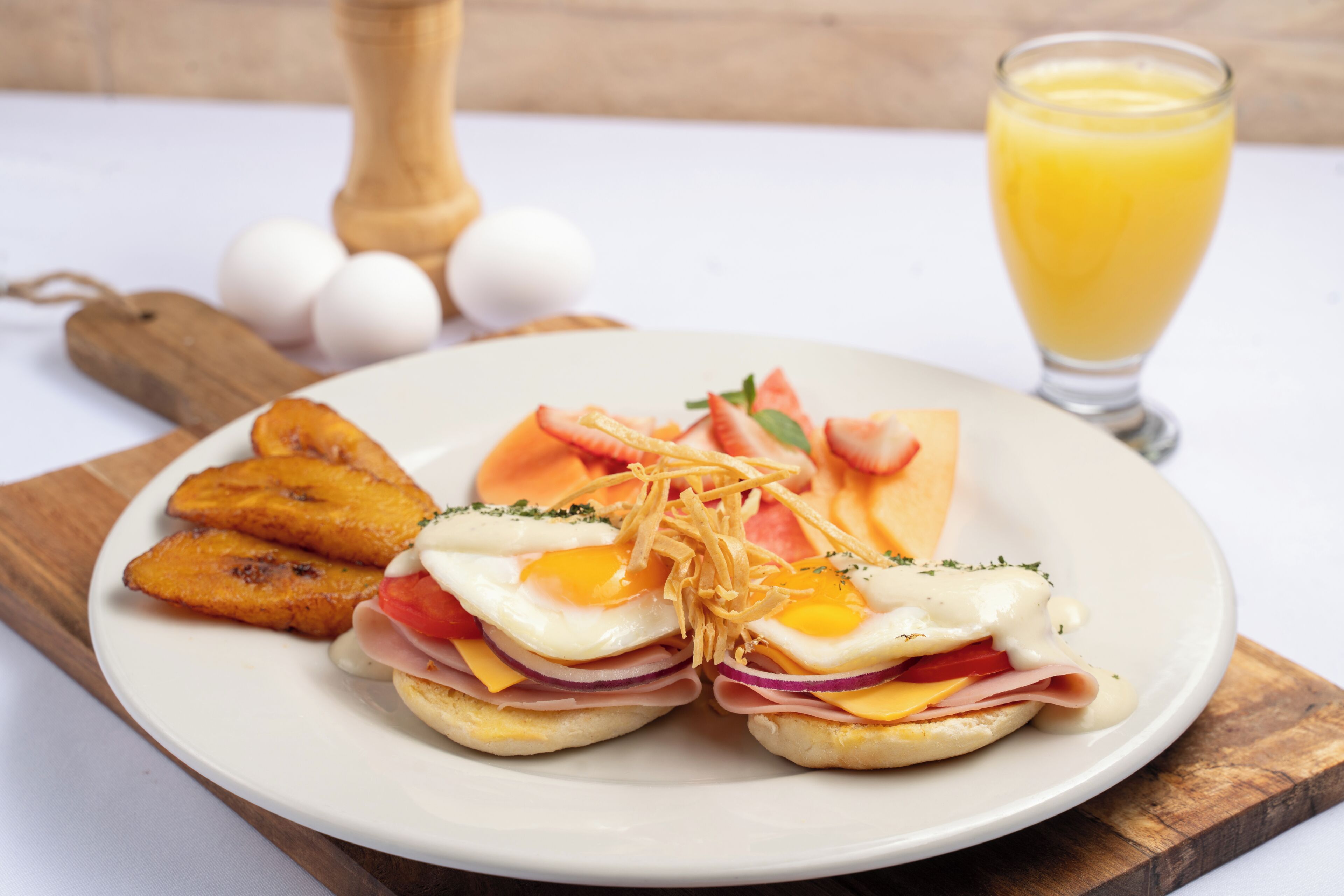 A plate with eggs, ham, cheese, and tomatoes, accompanied by fried plantains and a glass of orange juice.
