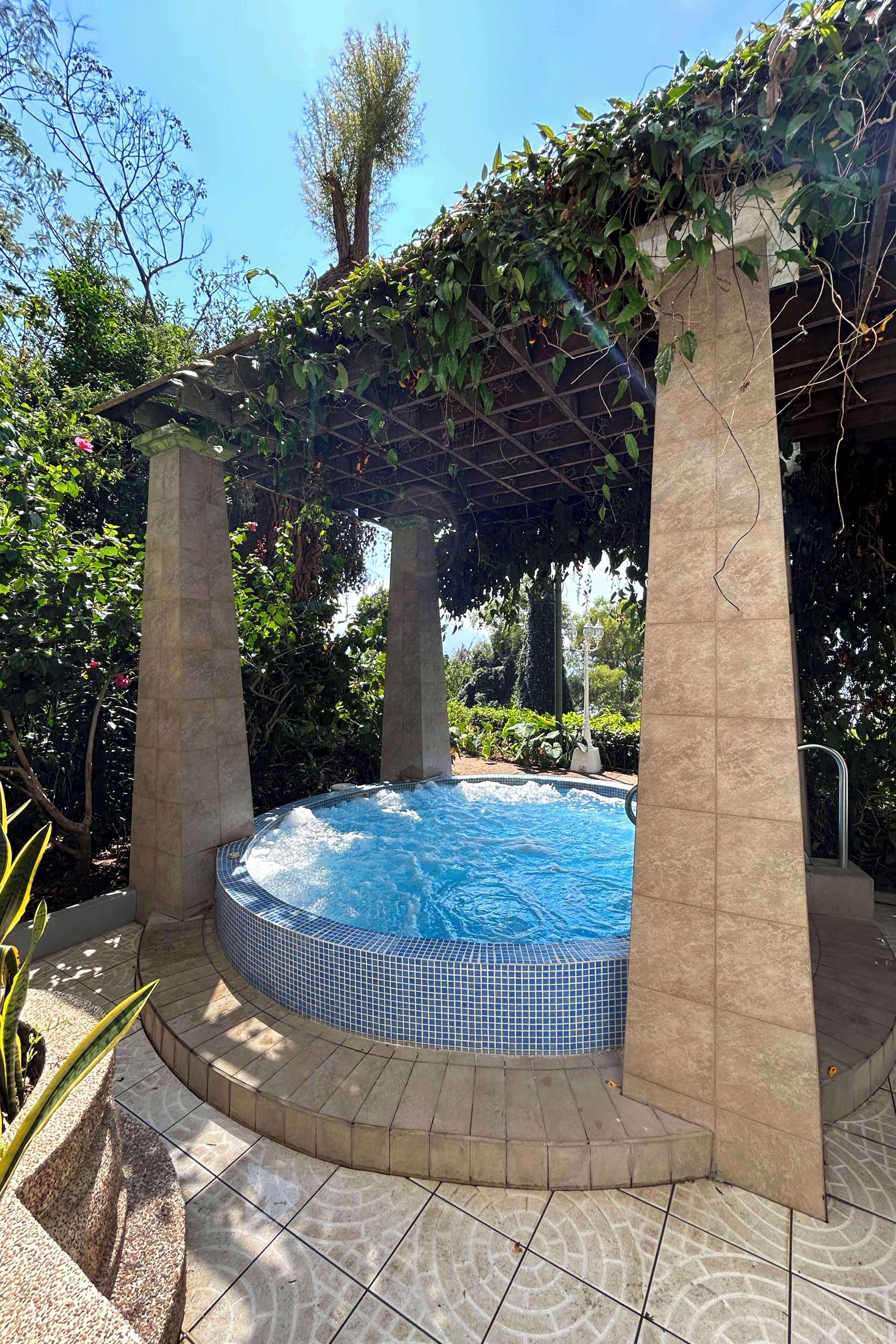 A hot tub surrounded by stone pillars, with a pergola overhead.