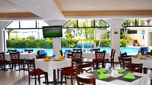 En restaurant med borde, stole, en tv-skærm og udsigt til en swimmingpool.
