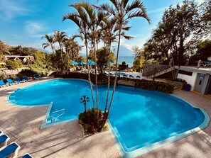 A swimming pool with lounge chairs, palm trees, and a view of the sea. - Hotel La Riviera de Atitlan (Sololá)
