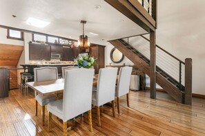 A modern kitchen with wooden flooring, a dining area with a table and chairs, and a staircase with a metal railing. - Deer Valley's Signature Collection (Park City)