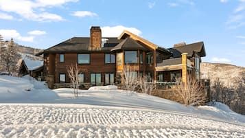A large wooden house with multiple windows and a balcony, surrounded by snow.