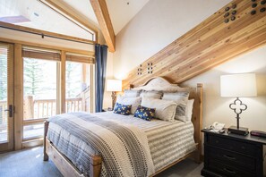 Camera da letto con struttura in legno, un letto grande, un comodino e vista sull'esterno.