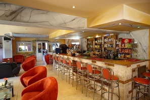Uma área de bar com teto de mármore, vários bancos altos e variedade de garrafas e petiscos nas prateleiras.