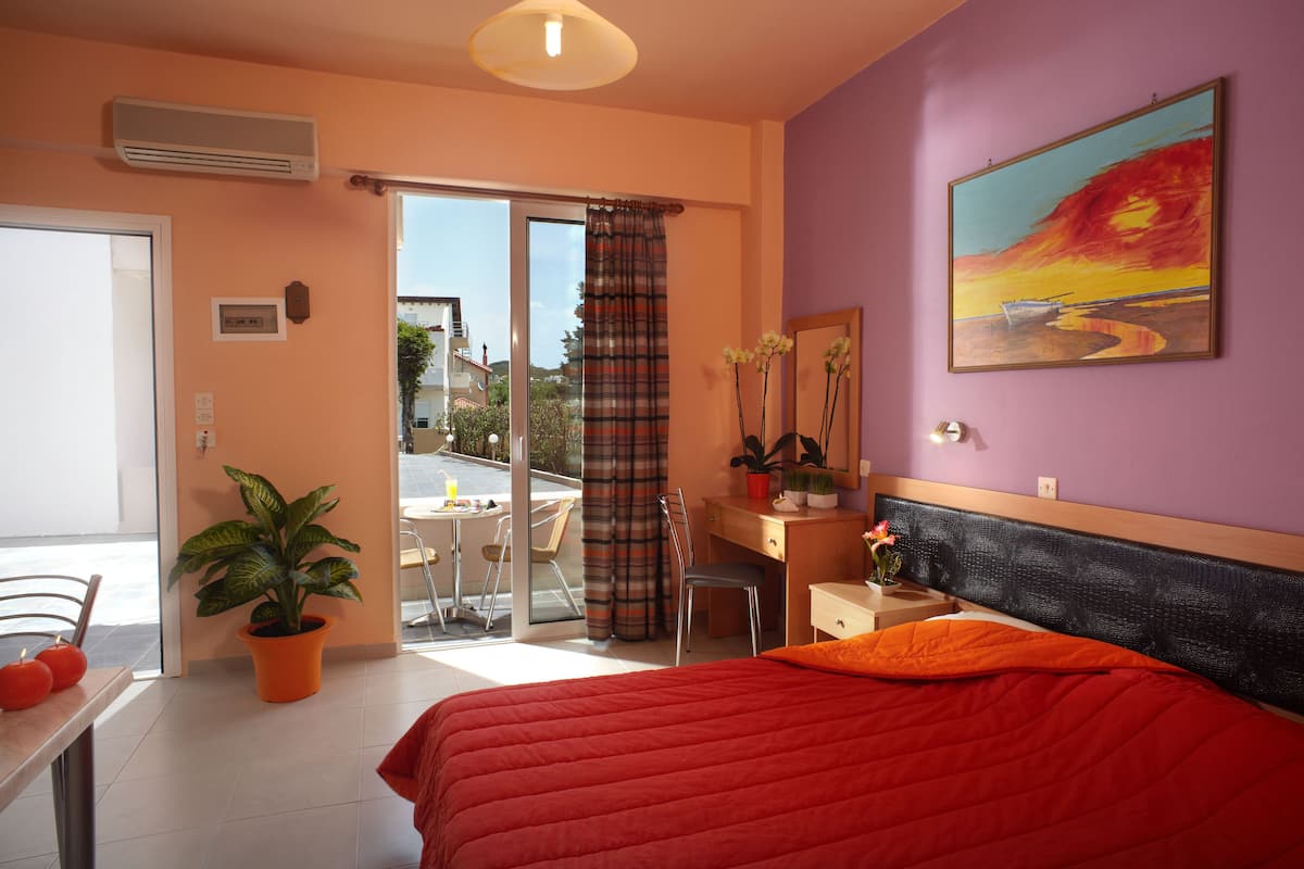 Un dormitorio con cama, escritorio, silla, planta en maceta y un cuadro en la pared.