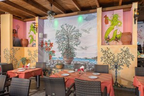 An outdoor dining area with wicker chairs and tables, decorated with murals and potted plants.