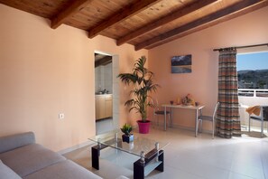 Uma sala de estar moderna com uma mesa de centro de vidro, um sofá, uma área de refeições com mesa e cadeiras, uma planta em vaso e vista para o exterior.