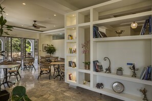 A spacious room with a large window, a ceiling fan, and a white shelving unit with books and decorative items. - La Signora Hotel (Kefalonia)