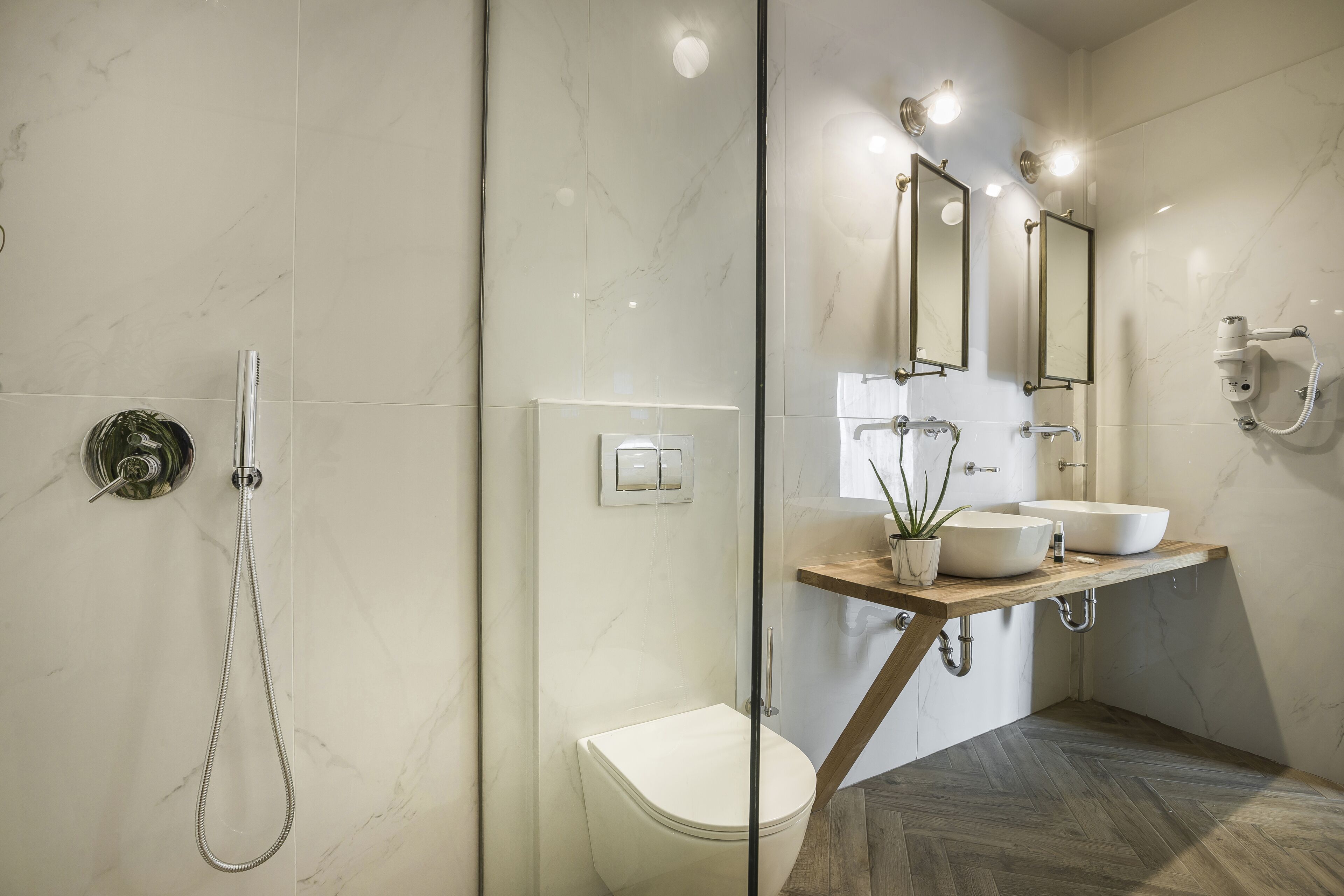 Een moderne badkamer met een douchecabine van glas, een wit toilet en een houten wastafelmeubel met twee wastafels.