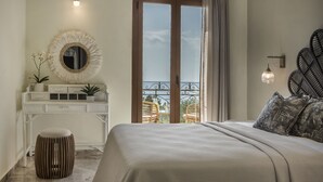 Un dormitorio con cama, cómoda, espejo redondo, taburete pequeño y balcón con sillas.