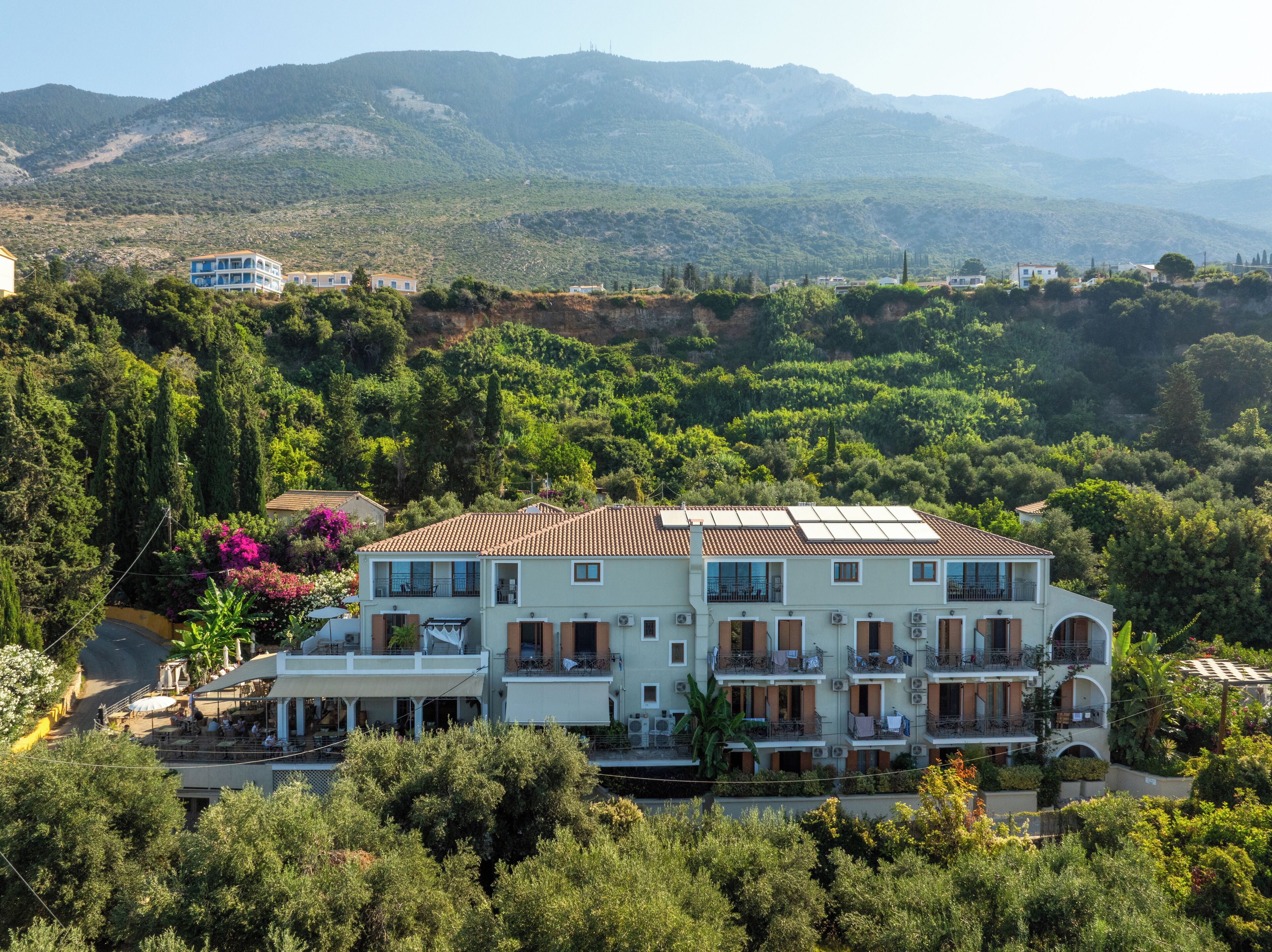 A multi-story building with a tiled roof, surrounded by lush greenery and hills in the background.