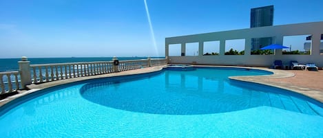 Una piscina al aire libre, sombrillas, sillones reclinables de piscina