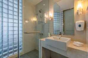 A modern bathroom with a glass shower enclosure, a white sink, and a hand dryer.