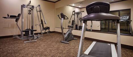 A hotel fitness center with cardio machines, weight machines, and a mirrored wall.