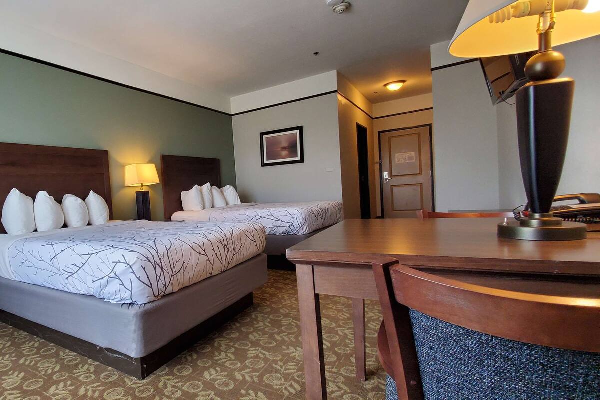 A hotel room with two beds, a desk, a lamp, and a framed picture on the wall.