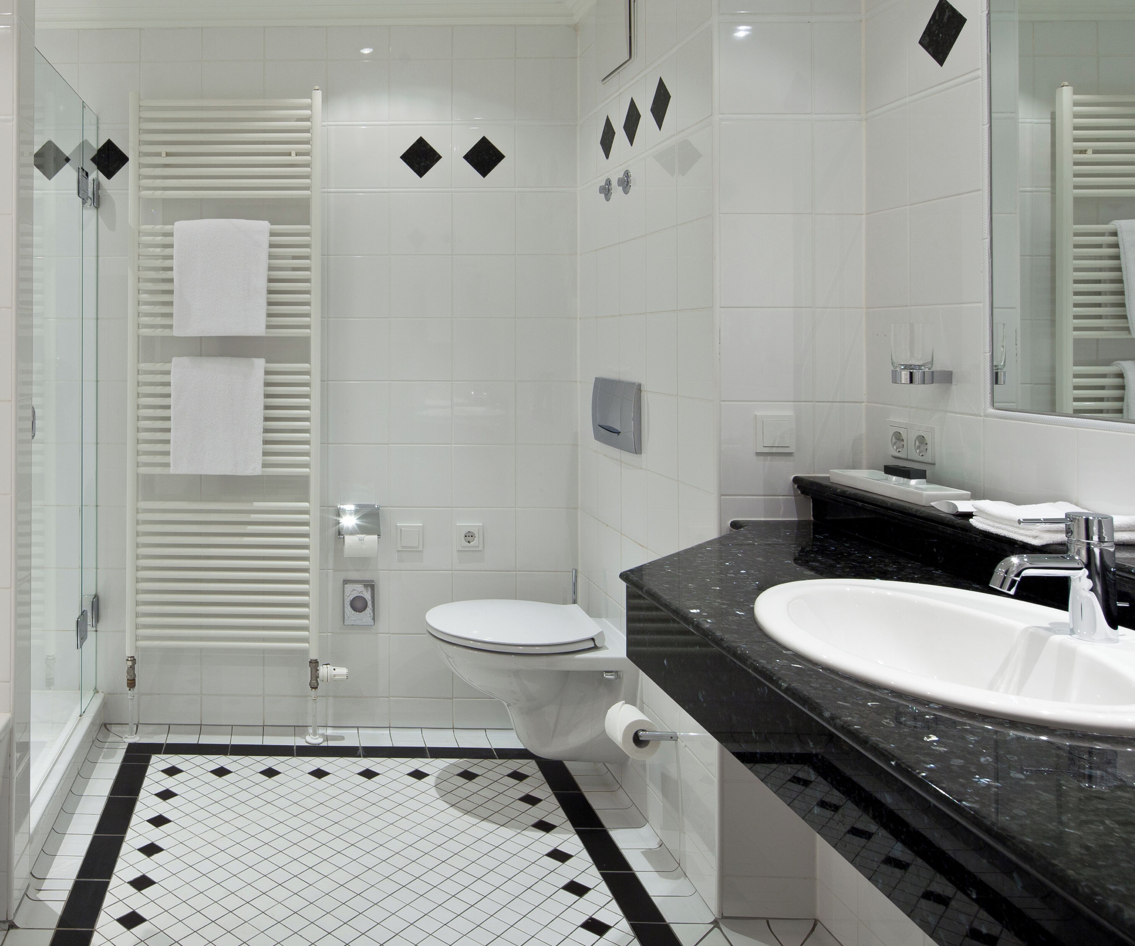 Ein modernes Badezimmer mit einer Duschkabine aus Glas, einer wei ßen Toilette, einem schwarz-weißen Fliesenboden und einer schwarzen Ablage mit einem weißen Waschbecken.
