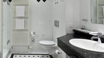 Um banheiro moderno com box de vidro, vaso sanitário branco, piso quadriculado preto e branco e bancada preta com pia branca.