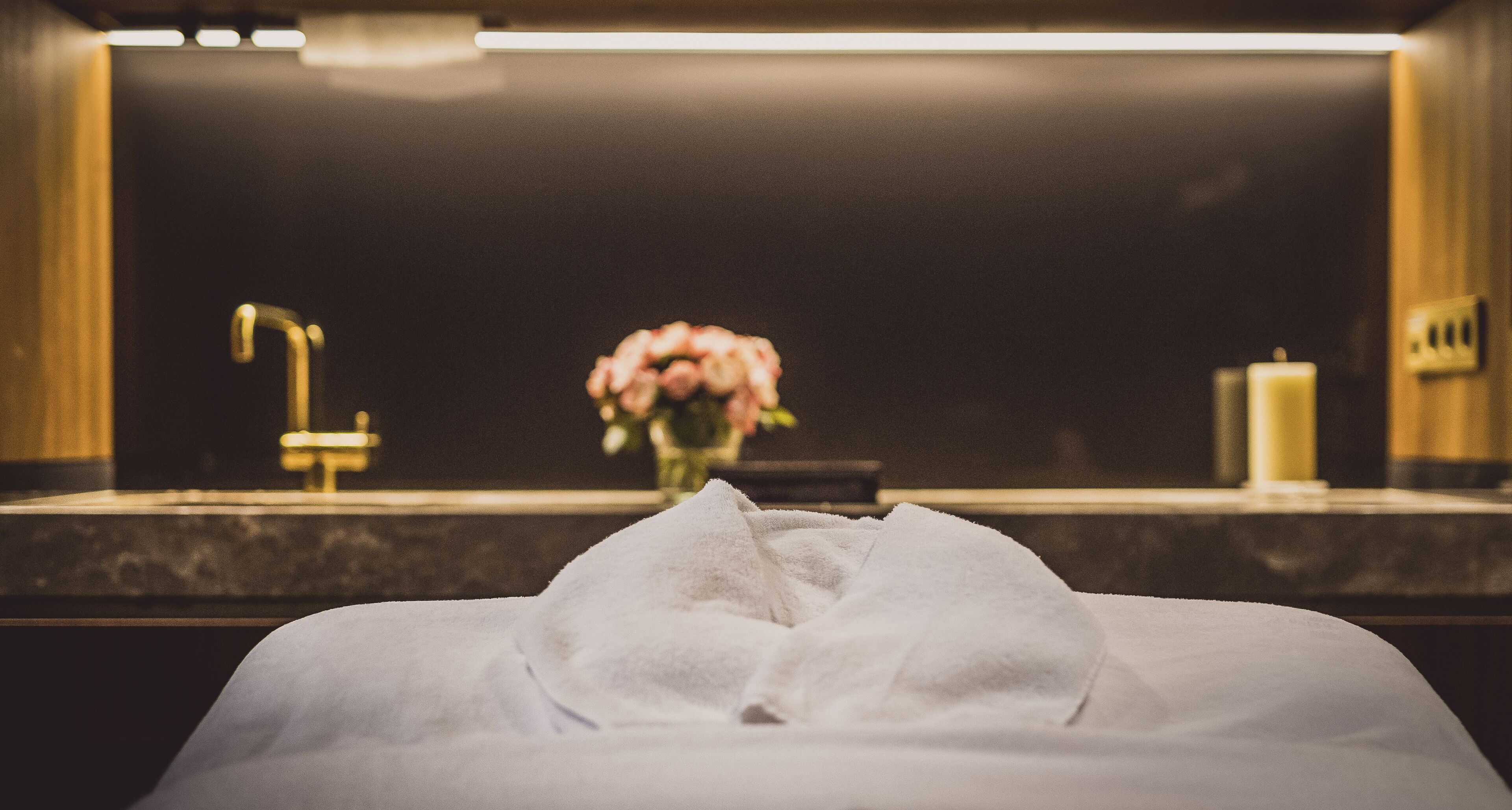 A hotel room with a bed, a bathroom with a mirror, a sink, and a vase with flowers.