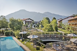 A pool area with lounge chairs and umbrellas, surrounded by greenery and overlooking a mountainous landscape.