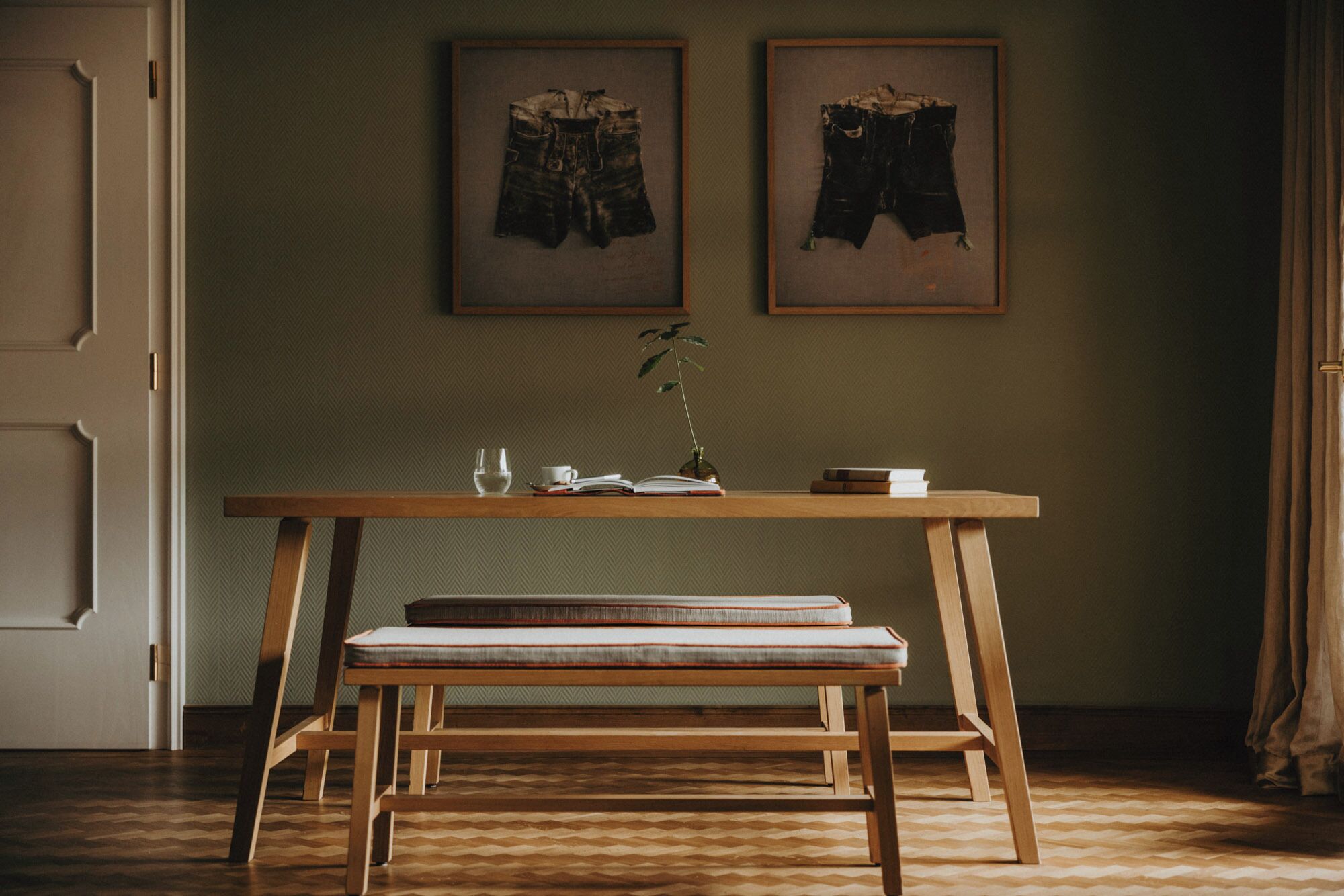 Una stanza con una panchina di legno, un tavolo con un vaso di fiori e due quadri appesi al muro.