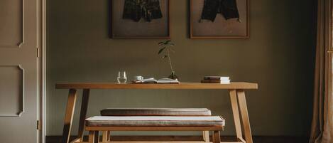 A room with a wooden bench, a table with a vase of flowers, and two framed pictures on the wall.