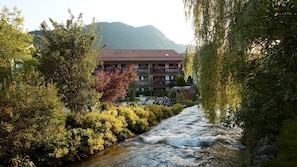 A hotel with a river running through its courtyard, surrounded by lush greenery and a mountain backdrop.