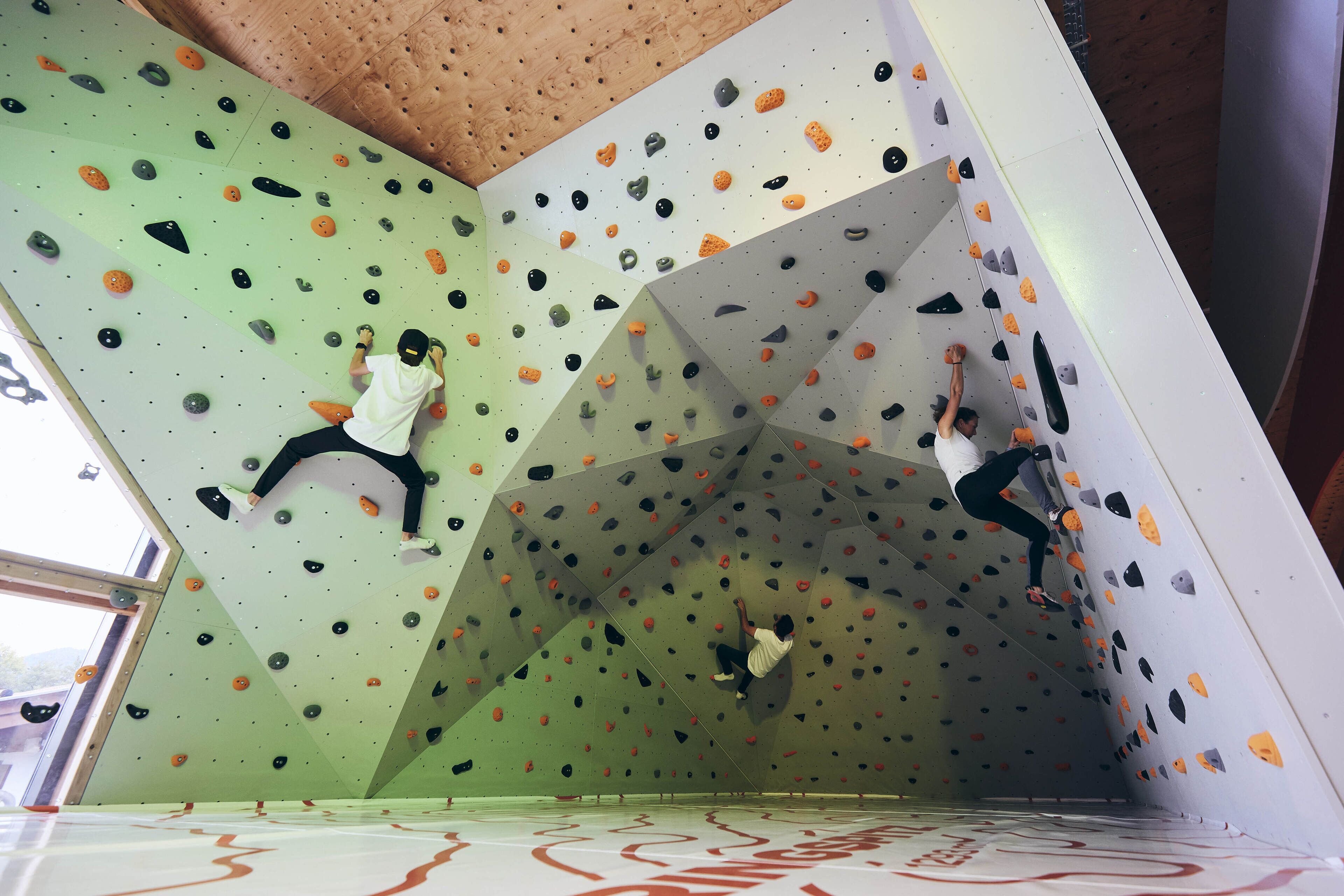Une salle d’escalade dotée de plusieurs murs d’escalade, d’un sol rembourré et d’un plafond au design géométrique.