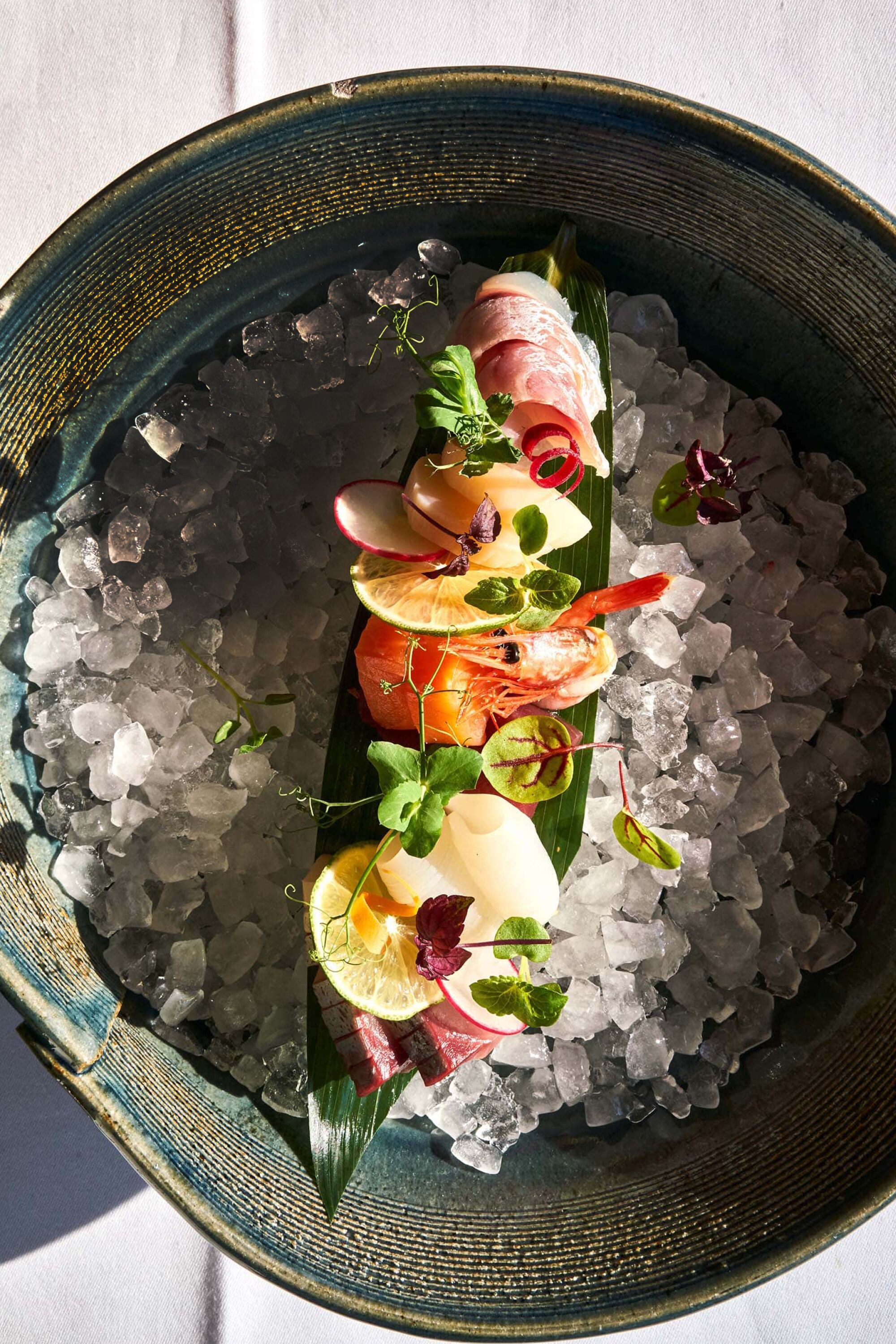 A seafood dish on a bed of ice in a ceramic bowl.