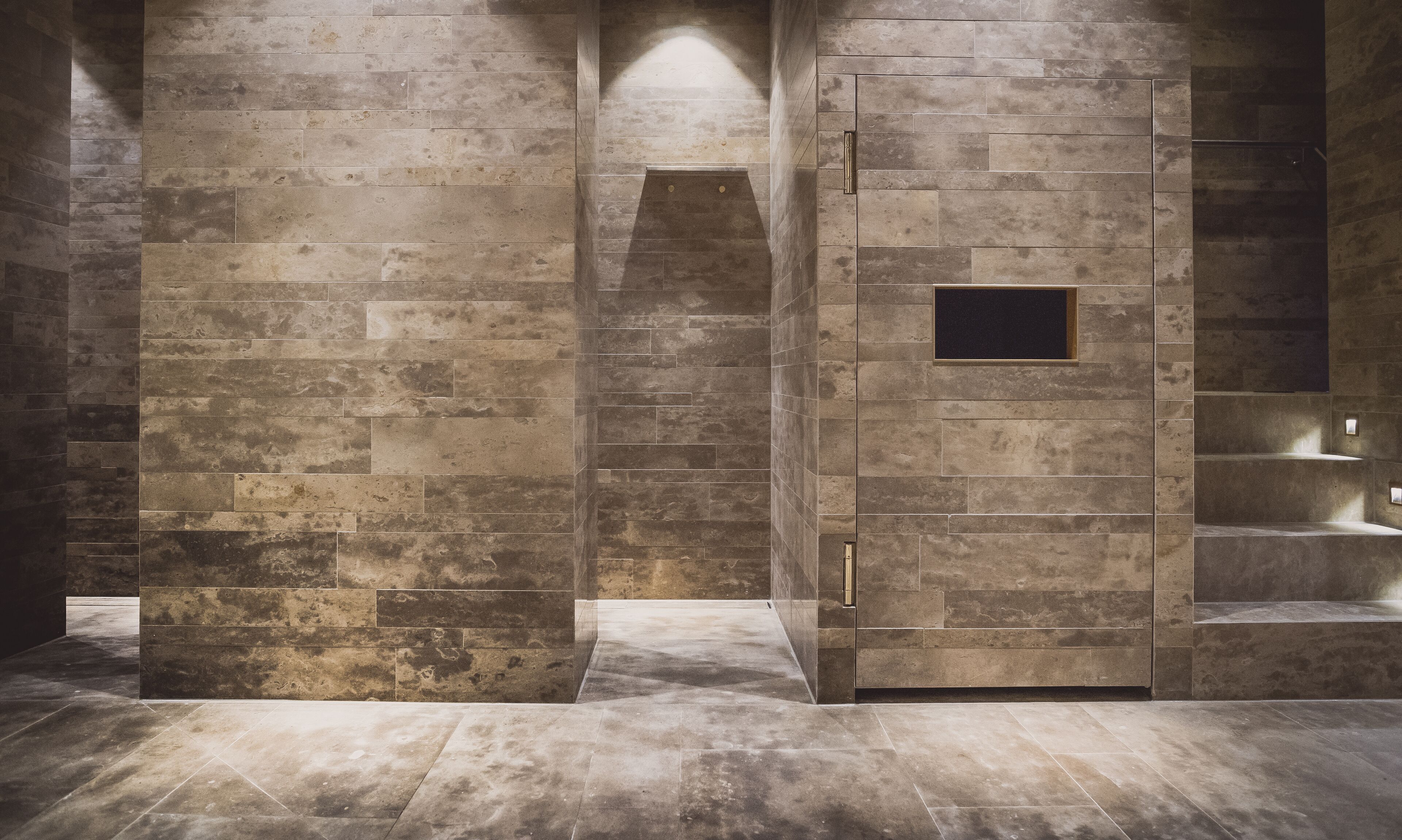 A modern bathroom with a stone wall design, a small window, and a built-in bench.