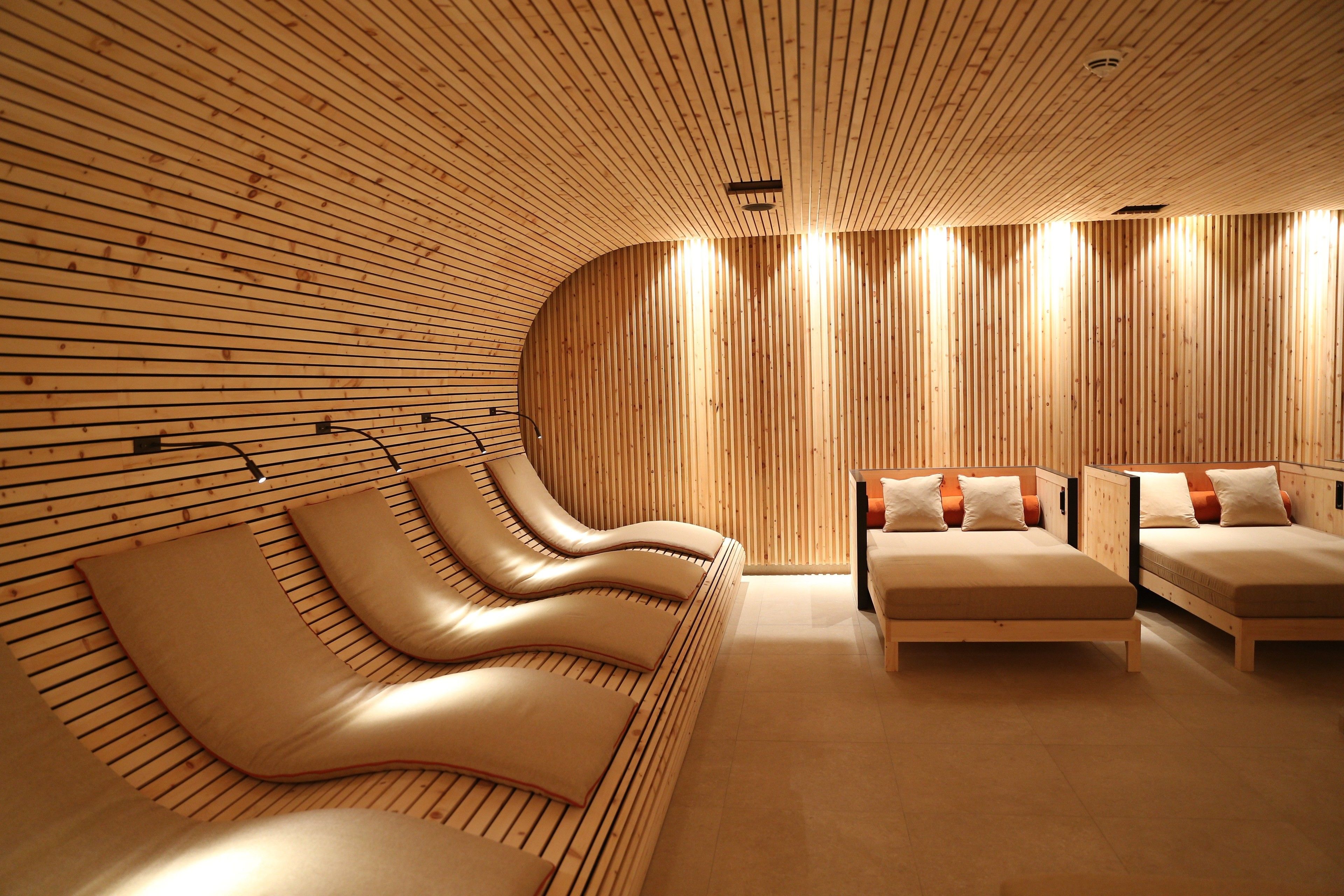 Un spa moderno con paneles de madera, techo curvo y varios sillones y camillas de masaje.