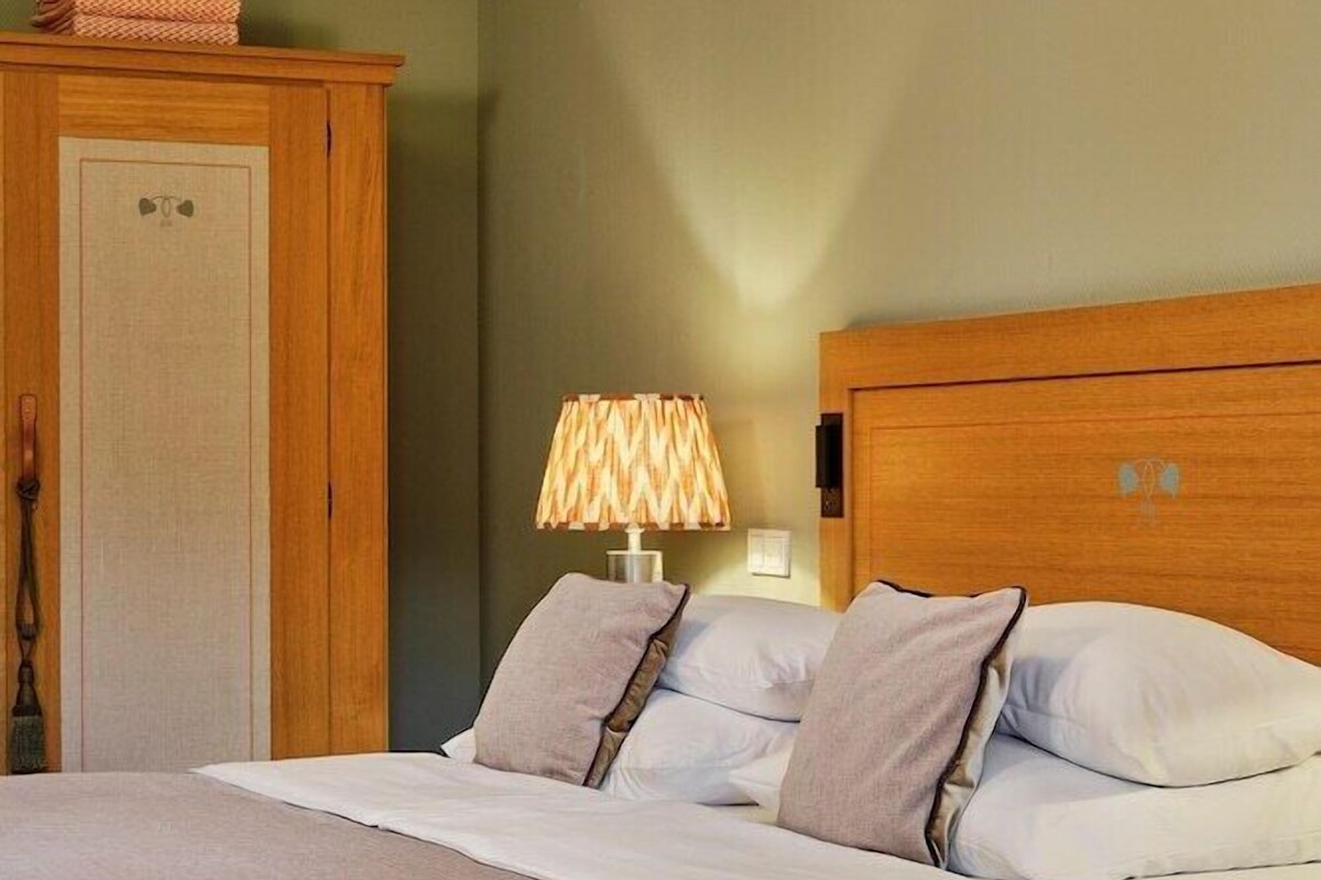 A bedroom with a bed, a wooden headboard, a nightstand with a lamp, and a wardrobe.