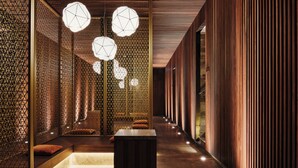 A corridor with a wooden floor, a central bench, and a patterned wall with hanging lights. - Spa & Resort Bachmair Weissach, LUXURY FAMILY RESORT (Kreuth)