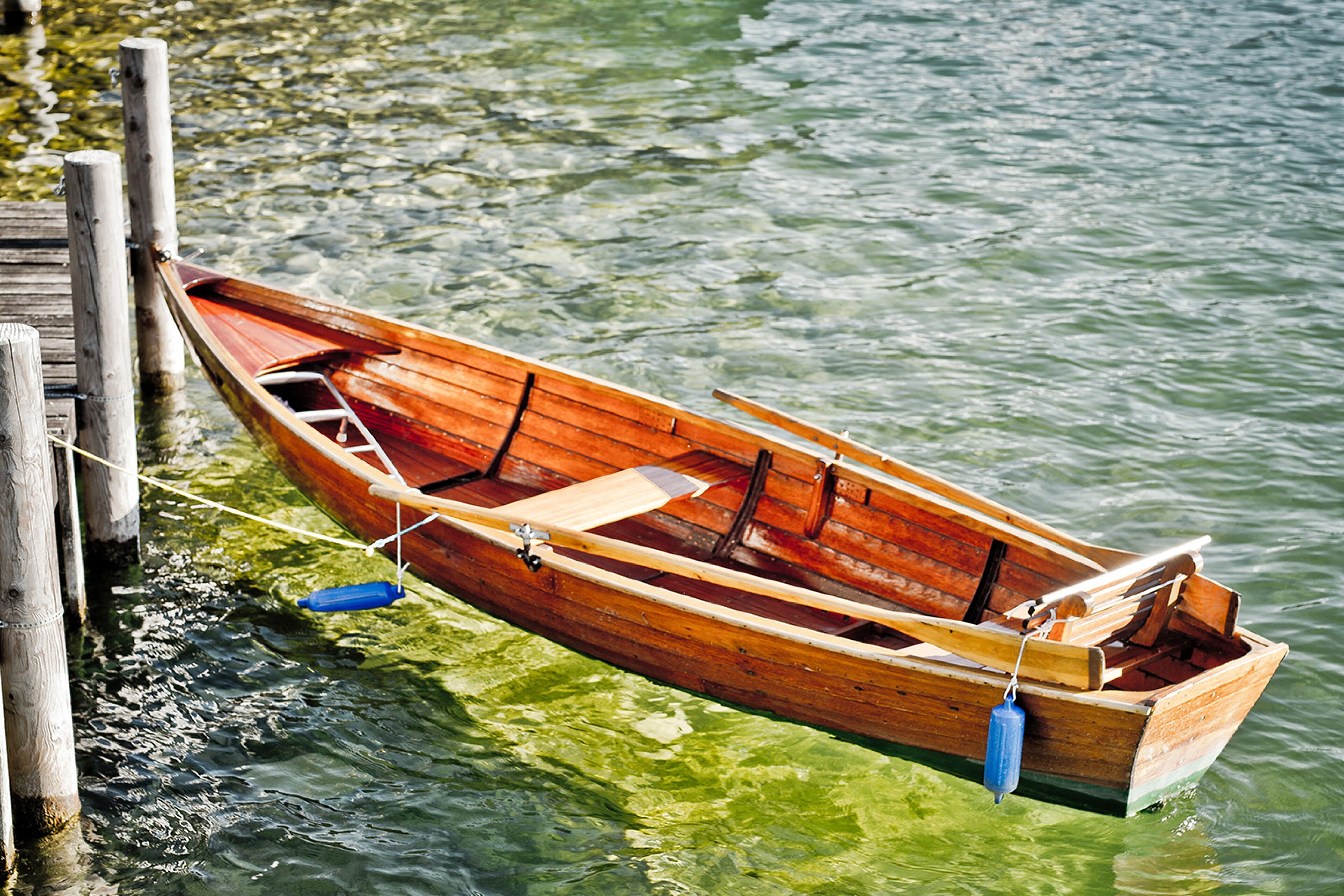 A wooden rowboat tied to a dock with a blue buoy.