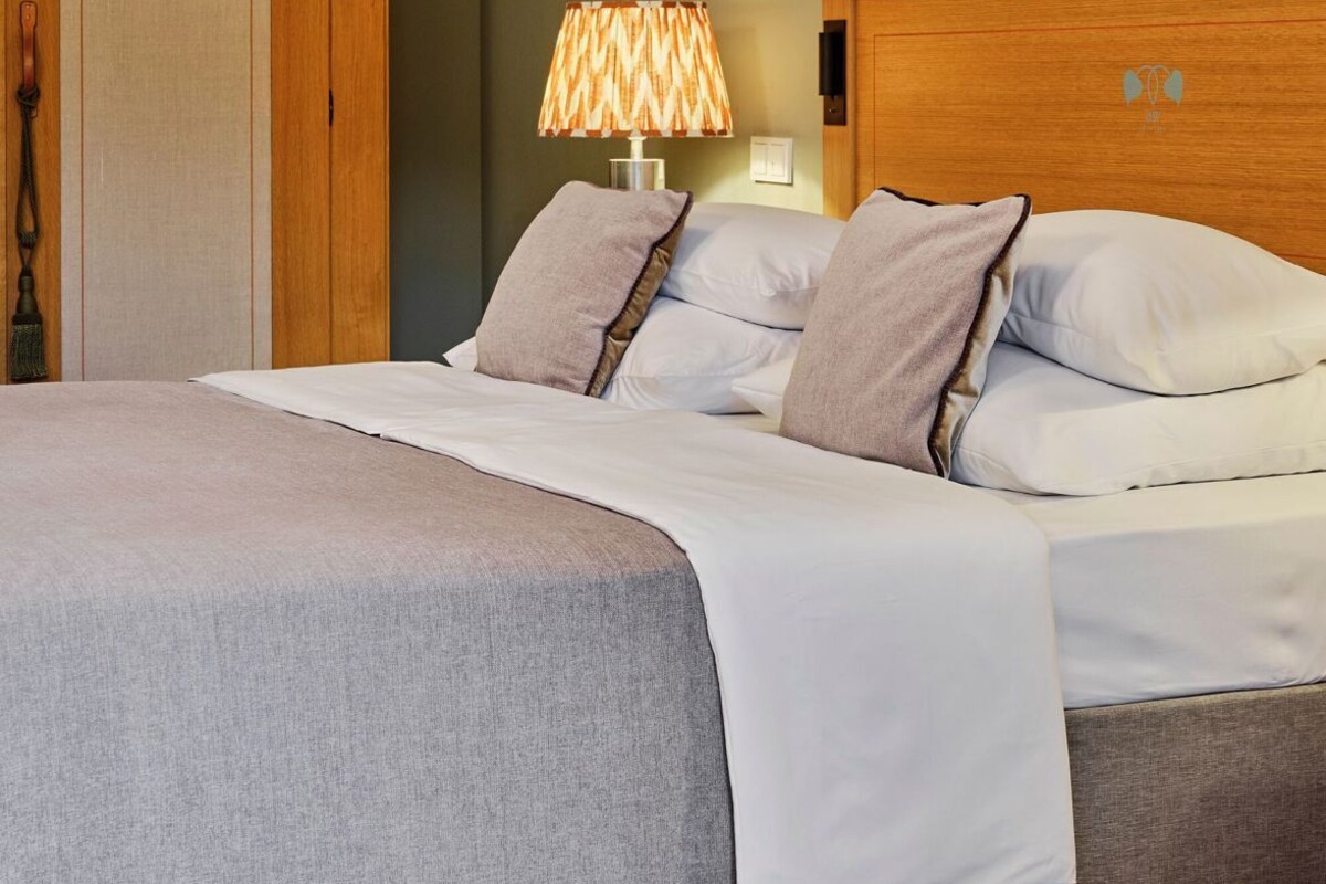 A neatly made bed with a headboard, a bedside lamp, and a wooden wardrobe in a room with green walls.