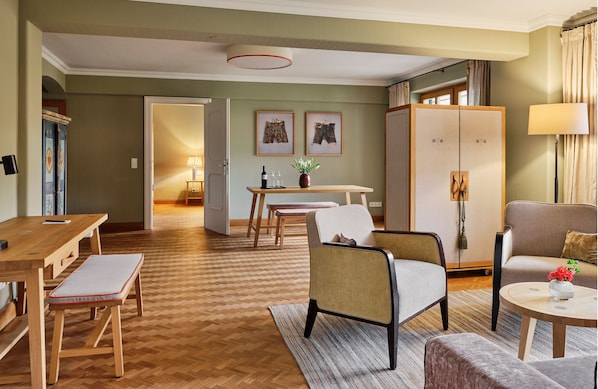 A hotel room with a wooden herringbone floor, a dining area with a table and chairs, a sofa, a cabinet, and a lamp.
