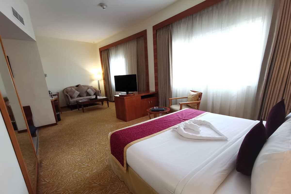 A hotel room with a large bed, a desk with a TV, a sofa, and a chair.