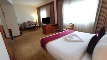 A hotel room with a large bed, a desk with a TV, a sofa, and a chair.