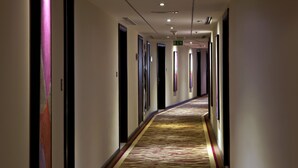 Un pasillo de hotel con alfombra estampada, puertas y un corredor que conduce a un área común.