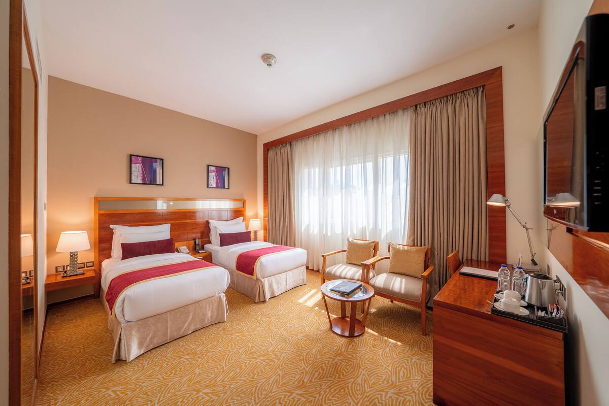 A hotel room with two beds, a desk, a chair, a small table, and a TV.