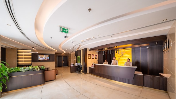 Un moderno vestíbulo de hotel con un mostrador de recepción, una señal de salida verde y una zona de recepción con dos empleados.