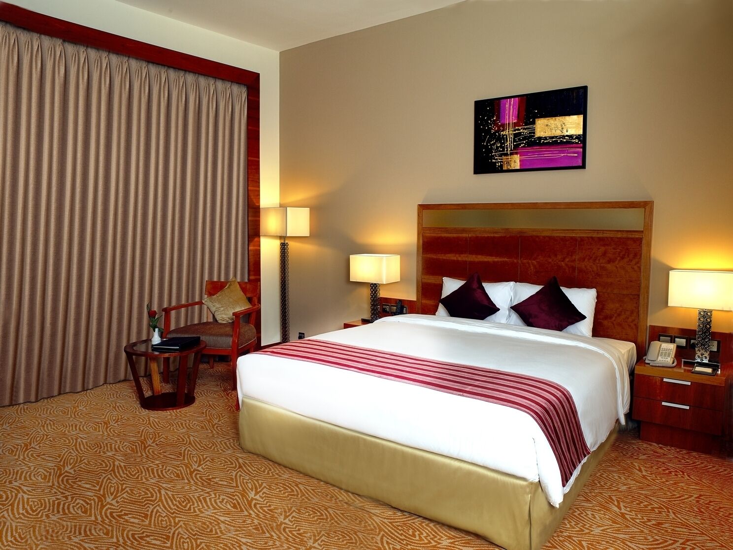 Une chambre d’hôtel avec un grand lit, deux tables de chevet, un bureau, une chaise, une lampe et un tableau au mur.