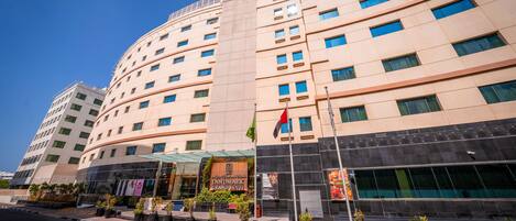 A multi-story hotel with a curved facade, large windows, and a prominent entrance with a sign.