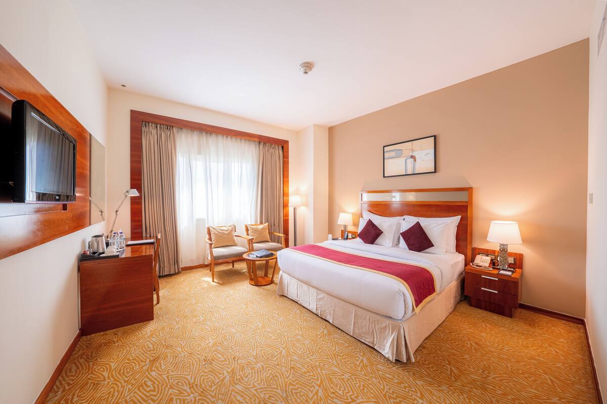 A hotel room with a large bed, a desk, a chair, a TV, and a window with curtains.