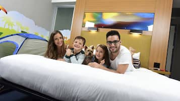 Una familia de cuatro personas en una cama con decoración de tienda de campaña, un cabecero de madera y un cuadro sobre la cama.