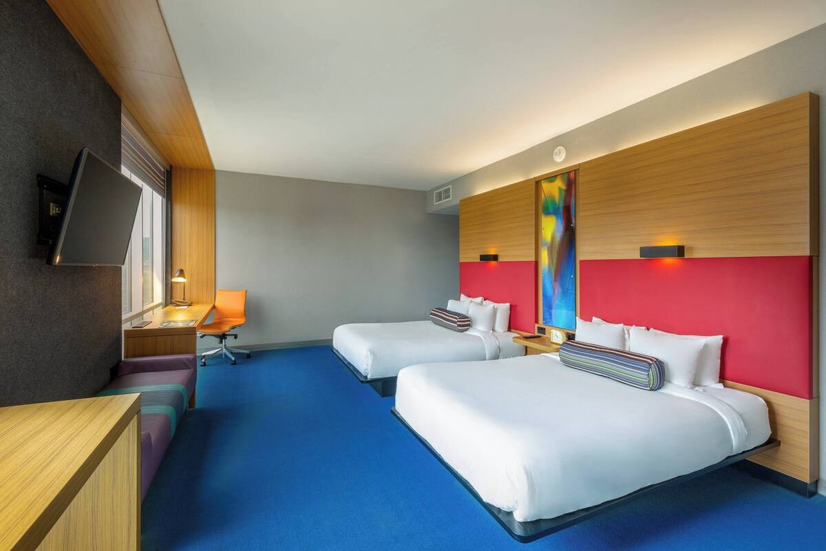 A hotel room with two beds, a desk, a chair, and a TV.