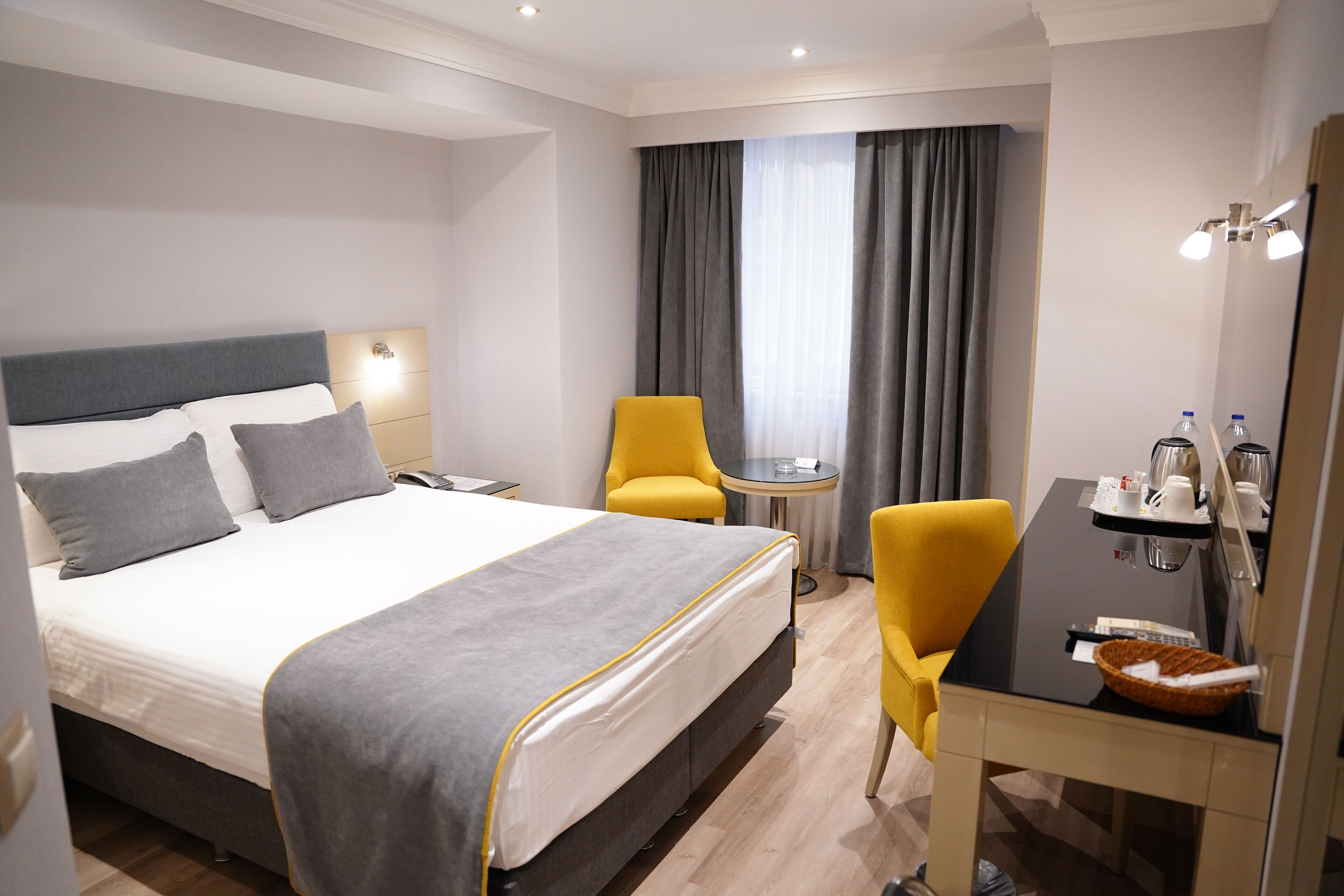 A hotel room with a large bed, two chairs, a small table, and a desk with a basket.