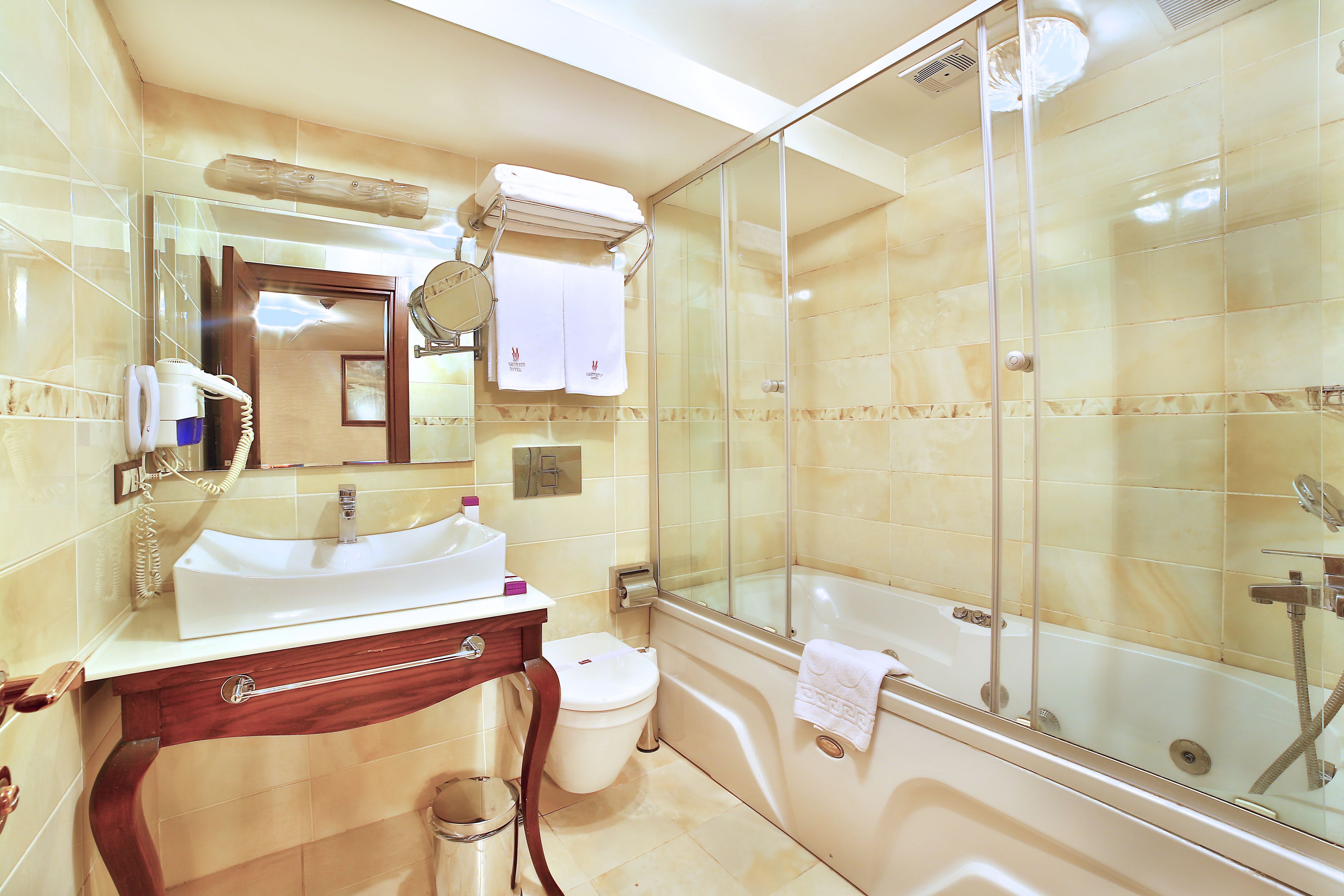 A bathroom with a glass-enclosed shower, a white sink, a toilet, and a vanity with a mirror and towel rack.